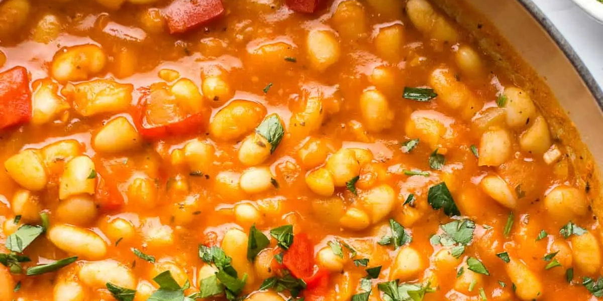 White bean stew in a ceramic pot with a wooden spoon stirring