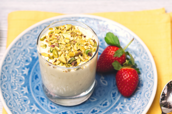 Berries and Pistachio Parfait Recipe Photo. Cup of yogurt is in a blue plate with some berries next to it; under the plate is a yellow napkin. Background is light grey.