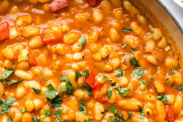 White bean stew in a ceramic pot with a wooden spoon stirring